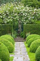 Formal garden with wooden pergola and climbing Rosa 'New Dawn', clipped Taxus and Buxus hedging with view to stone statue