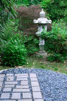 Slate chippings and paved area, stone temple ornament amongst shrubs in oriental style garden - Jardin de Valérianes, France