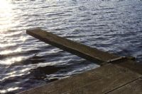 Wooden jetty and diving board with setting sun reflected in lake
