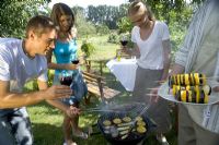 Couples cooking fish and vegetable kebabs on barbecue in garden