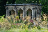 Mixed perennials and ornamental grasses including Stipa gigantea, Achillea and Echinacea with view to stone loggia - The Italian Garden at Trentham, designed by Tom Stuart-Smith