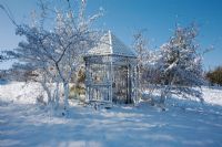 Fresh covering of snow on a rustic wooden gazebo in country garden with Fraxinus trees