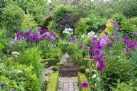 Brick path and sundial surrounded by borders with alliums including Allium hollandicum at Dial Park, Worcestershire.