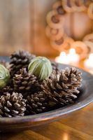 Festive arrangement of pine cones and dried limes in wooden bowl with candles in the background