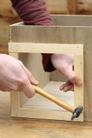 Step by step 4 of making a hedgehog house - Nailing trim around entrance hole to wooden box