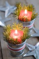 Red candles in mini zinc buckets with fir tree foliage and ribbon as a table decoration.