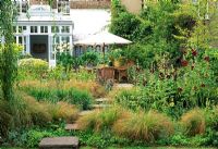 Raised pavers lead back towards the house and dinning area in this London garden, over this planting of Stipa arundinacea, ruby red holly hocks and yellow Phlomis russeliana.