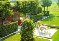 This aerial view reveals the layers and divisions of this otherwise flat Belgium garden. Pleached hornbeams and hedging screens the garden room from the dinning terrace. Limestone blocks raise and border the lawn. A climber covers a metal structure adding another geometric feature to the garden.
