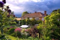 The house from the upper garden with stormy sky, planting includes Magnolia x loebneri 'Leonard Messel', Physocarpus diabolo and Cynara cardunculus - Mariners Garden, Berkshire
