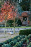 Autumn colour in the walled garden - the garden of spheres with wooden gate in wall, stone ball and Amelanchier x grandiflora 'Robin Hill' - Marks Hall, Essex