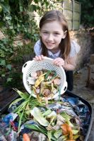 Girl emptying plastic colander with food waste in to the compost bin