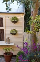 Summerhouse with baskets of Vinca minor 'Illumination' and Eryisumum 'Bowles Mauve' in border