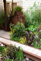 Detail of planting including Arundo donax, Calamagrostis x acutiflora 'Karl Foerster', Carex elata 'Aurea', Darmera peltata, Deschampsia cespitosa, Eupatorium purpureum, Ligularia dentata 'Britt Marie Crawford', Ligularia przewalskii, Lysimachia, Lythrum, Persicaria affinis 'Superba', Phormium tenax 'Dusky Princess' and Spartina pectinata 'Aureomarginata' in 'The Rain Chain' sustainable garden at RHS Hampton Court Flower Show 2009