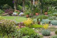 View of secluded back garden with raised lawn, pond planted with Nymphaea - water lily, Iris pallida 'Variegata', Carex elata 'Aurea' and Myriophyllum, with adjacent 'beach area' with Thymus serpyllum 'Coccineus', Lavender 'Hidcote', Dianthus and Osteospermum. Beyond pergola with Clematis jackmanii 'Superba', Rosa 'Compassion' and purple foliage bed with Cotinus coggygria 'Royal Purple', Pittosporum 'Tom Thumb', Berberis thunbergii 'Atropurpurea Nana', Cineraria maritima, Astilbe simplicifolia 'Sprite' Alstroemeria 'Devotion' and Campanula persicifolia alba. Gorse Way, NGS garden, Lancashire