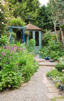Paved and gravel curved path leading to green painted summerhouse in densely planted tiny courtyard garden