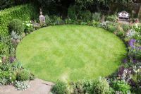 Overview of small Urban garden packed full of plants simply designed around a central circular lawn