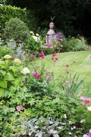 Small Urban garden packed full of plants simply designed around a central circular lawn. Flower border surrounding circular lawn with focal point sculpture by Christopher Marvell, Hydrangea arborescens, Knautia macedonica, pink Astrantias, and Iris foliage.