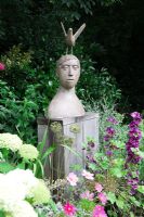 Small urban garden packed full of plants. Sculpture by Christopher Marvell on oak plinth, surrounded by Hydrangea arborescens 'Annabelle', Cosmos bipinnatus 'Sensation', Malva sylvestris 'Mauritanicus' and Allium seedheads.