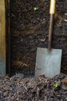 Garden spade next to garden compost heap showing different layers of rotted plant material
