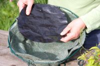 Planting up a hanging basket - adding a plastic disc to the fibre liner
