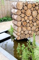 Log wall made from sustainable recycled timber and small pond. Future gardens, St Albans, Herts. 'Narratives of Nature' garden.