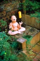 Raised bed with laughing Buddha sculpture on gravel - After makeover of a Brixton garden for Channel 4 Garden Doctors 