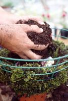 Planting a hanging basket step by step. Stage 6. Fill the bottom half of the basket with compost. Mix in water retaining gel and slow release fertiliser into the compost.