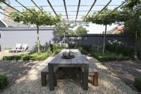 Urban meditation garden. Bamboo pergola with trained Platanus hispanica creates a roof over dining area. Buddha and candles on the table. Two Pyrus communis and Hydrangea 'Annabelle' near grey wall. 