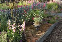 Colourful summer raised bed by picket fence with Lavandula, Verbena, Penstemon, Diascia and Anthemis. Brick inlay for pots. 'Hazelwood', Jacqueline Iddon Hardy Plants, NGS garden, Lancashire