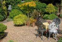 Decorative metal table and chairs in summer gravel garden at 'Hazelwood', Jacqueline Iddon Hardy Plants, NGS garden, Lancashire 
