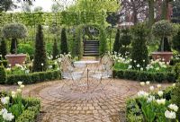 Parterre with Buxus edged beds of Tulipa 'Spring Green', Florosa', 'Groenland' and 'Super Parrot', Yew pyramids and standard variegated Holly trees, rusted iron chairs and table on circular patio - Northend