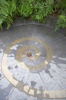 Slate and stone 'Ammonite' pattern flooring with central drainage surrounded by ferns