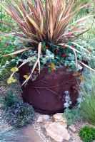 Planter with Phormium 'Pink Panther', Geum 'Cooky', Helichrysum petiolare 'Silver', Lotus berthelotii 'Fire Cracker', recycled crushed ceramic gravel planted with Thyme and Eryngium bourgatii - 'The Fire Pit Garden' - Silver Medal Winner at the RHS Hampton Court Flower Show 2010 
