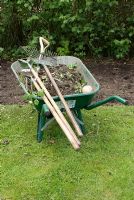 Wheelbarrow full of weeds and tools beside cleared border 