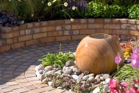 Circular cobble sett path with central stone sphere water feature and brick wall with raised bed. Southport Flower Show 2010