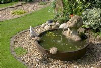 A half barrel water feature with submerged head water spout and hands, sunk in gravel bed with stone sett edge at 'Trevinia', Stubbins, Lancashire NGS