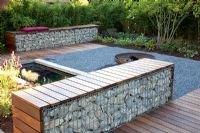 Small garden with patio, pond and benches made from wood and gabions backed by Fargesia murielae - Bamboo hedge
