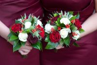 Wedding bouquets of red roses, white roses, Eryngium and berries held by bridesmaids