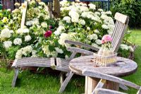 Wooden recliners and table near flowerbed with Hydrangea arborescens 'Annabelle' 