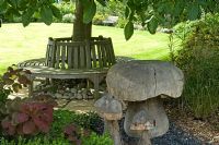 Circular bench under tree and wooden ornamental mushrooms. Parsons Cottage, Essex, UK