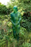 Green resin sculpture figure in border with Angelica and Prunus - Cherry tree. Yulia Badian garden, London, UK
 