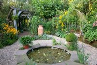 Small pond on gravel patio with decorative arbour and pot plants