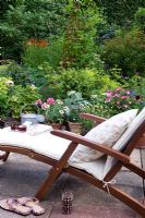 Reclining steamer chair with cushion on terrace overlooking garden border 