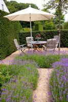 Gravel path to seating area in garden with Lavandula angustifolia - Lavender.
