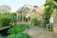 Timber decking, pond and conservatory. Wooden bench and Agave in container. Late Spring, Fovant Hut Garden, Wilts
