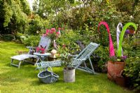 Loungers on lawn next to border with Rosa and colourful ornament made from strips of fabric in terracotta pot
 
