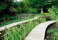 Raised boardwalk winding through bog garden, bridge over river leading to summerhouse - Weir House, Hants