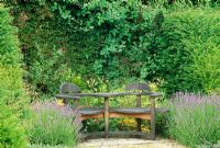 Wooden seat, designer Matthew Burt in border with Lavandula, Lilium and topiary yew - Weir House, Hants