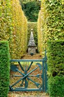 Blue gate leading to clipped Fagus and Taxus baccata hedges and stone obelisk - Silverstone Farm, Norfolk
