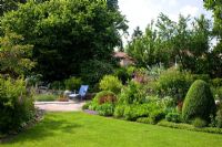 View from a lawn to a blue deckchair on a flagstone area. Planting includesRosa 'Sibelius', Berberis thunbergii 'Atropurpurea', Buxus, Corylus avellana, Pyrus salicifolia, Spiraea thunbergii and Tanacetum parthenium